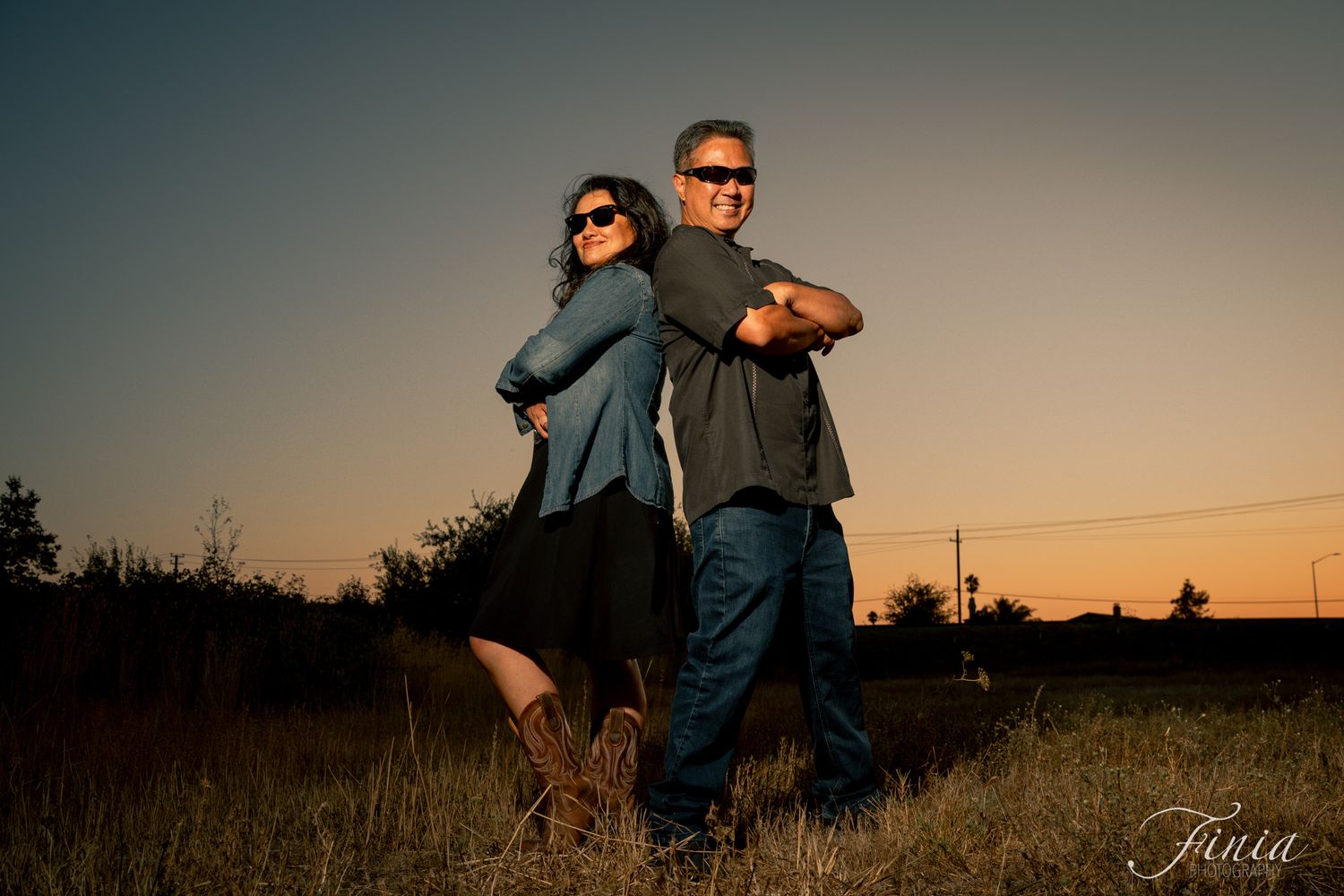 A romantic couple stands silhouetted against a warm sunset sky in a scenic outdoor setting.