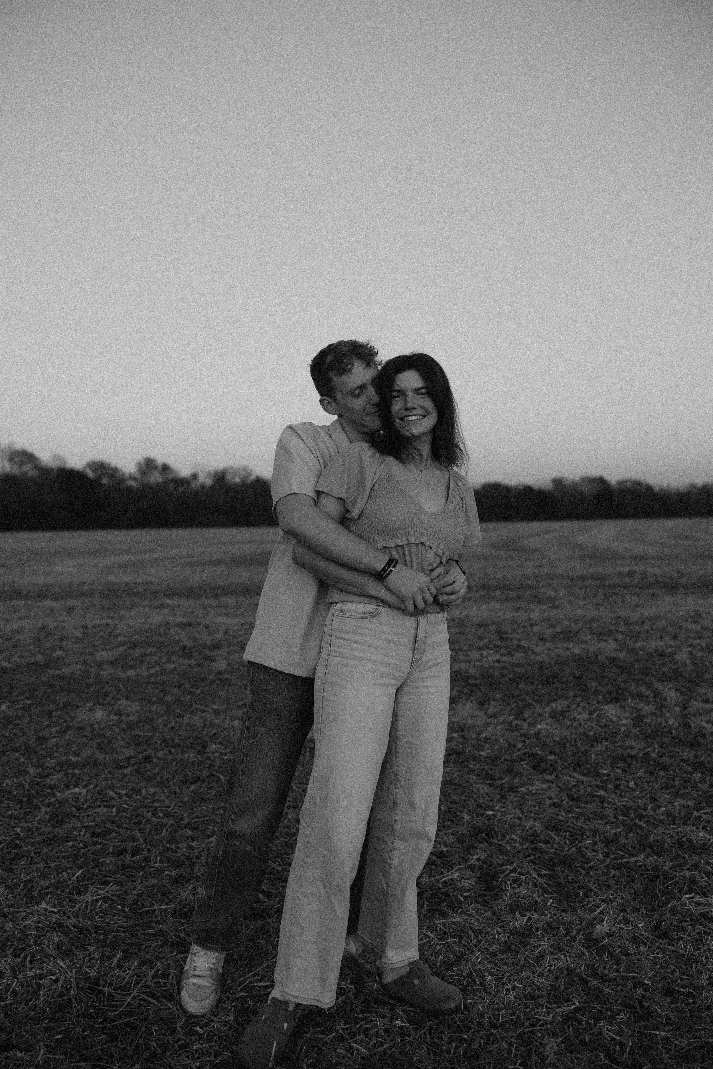 Couple embracing in an open field during a black and white photoshoot.