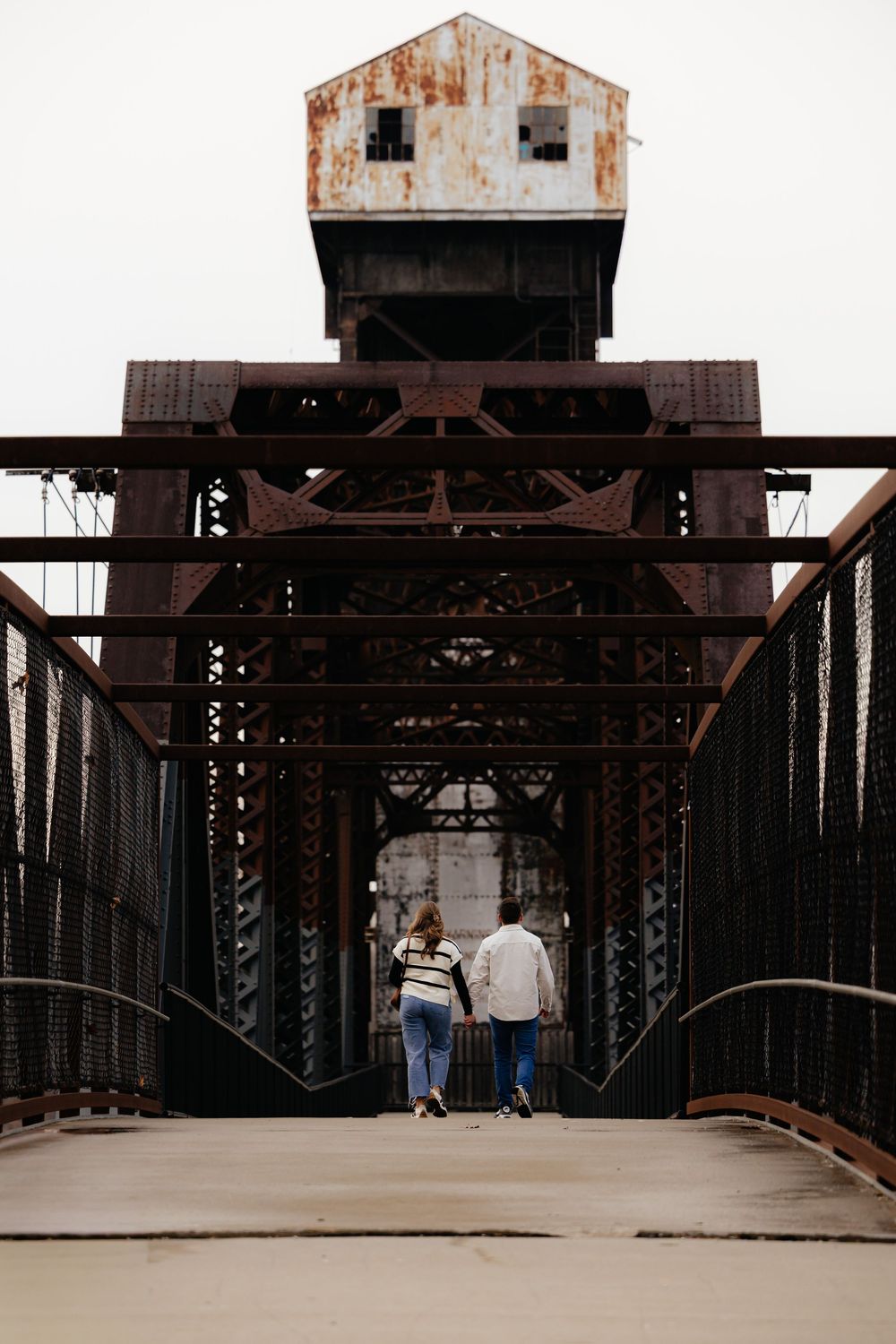 People walking across a rustic steel bridge with industrial metal framework.