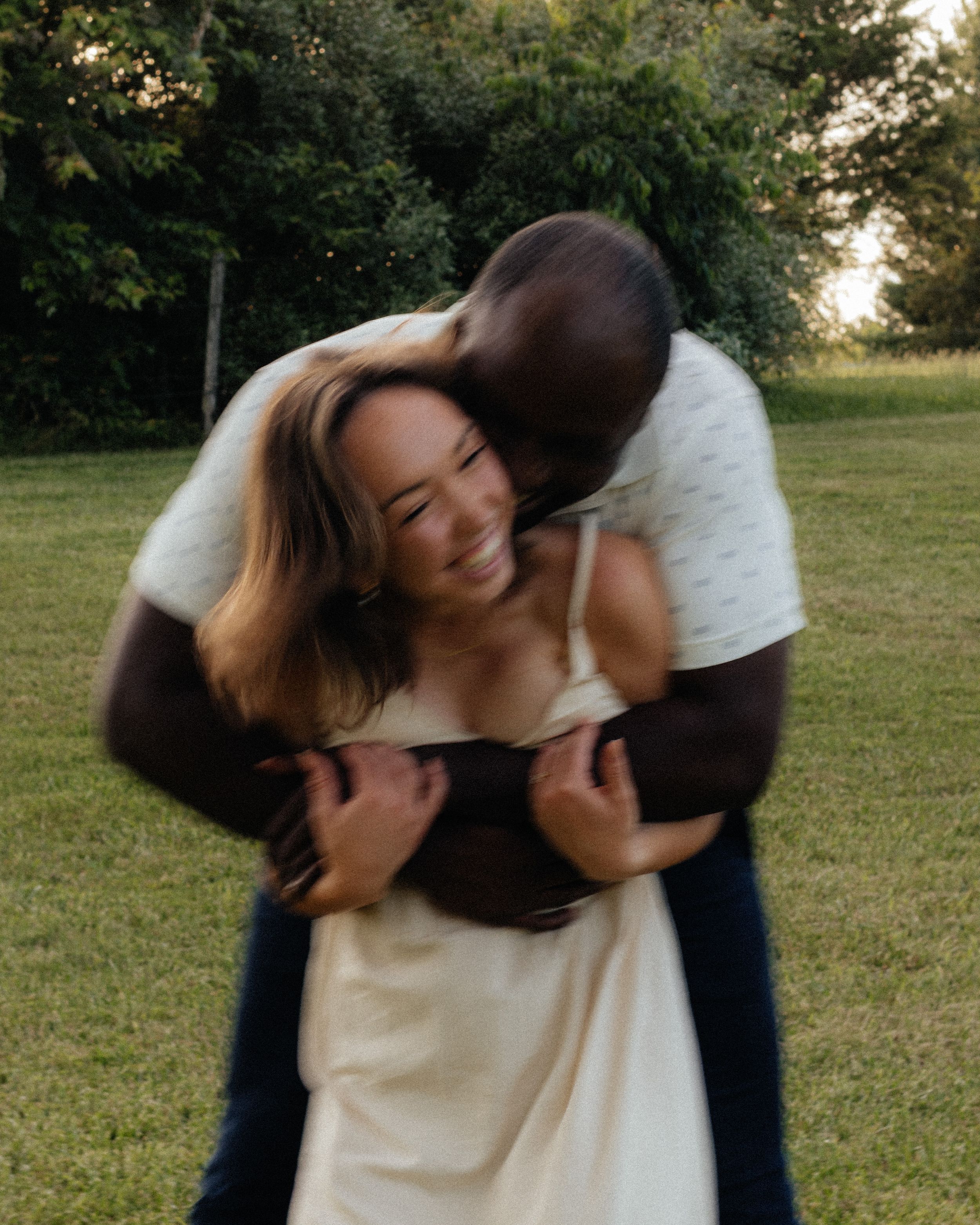 Joyful embrace between couple in white clothing on grassy field.