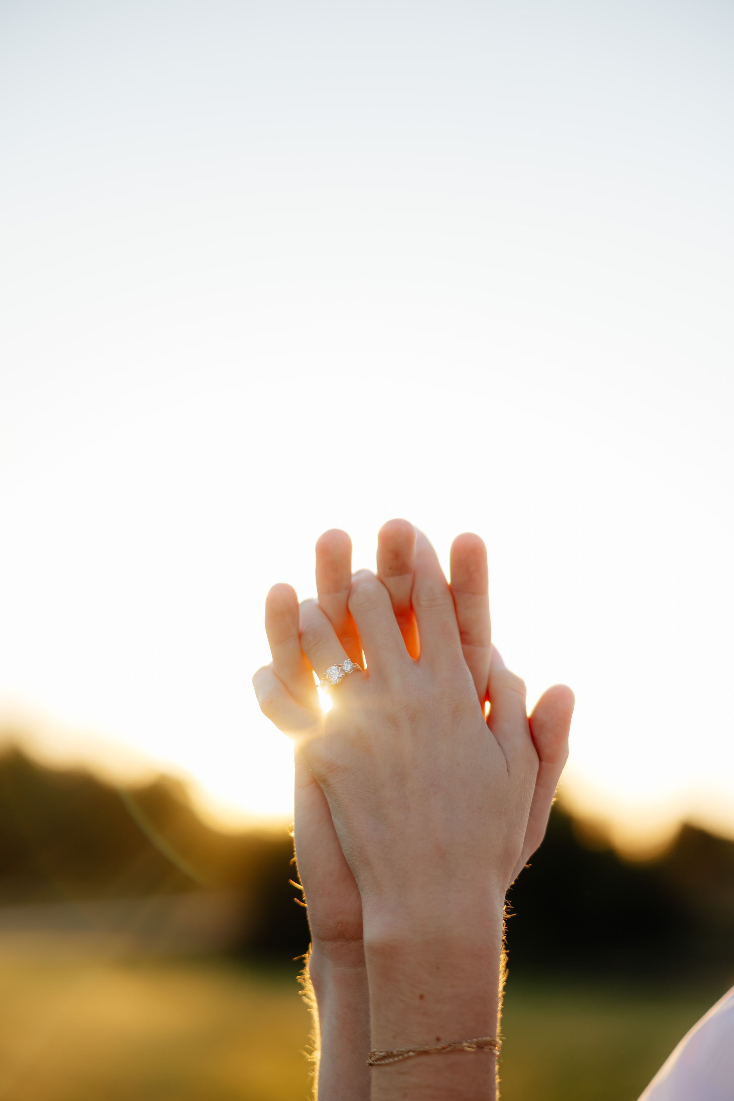 Hands clasped together against sunset sky creating silhouette with sunlight streaming through fingers.