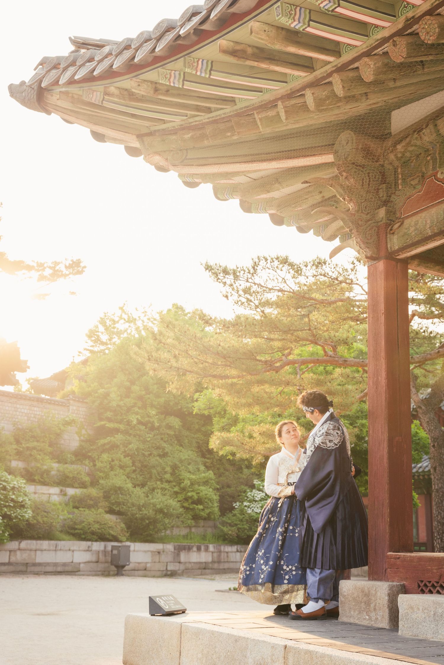 Traditional Korean pavilion with wooden architecture and tiled roof during golden sunset hour at historic palace grounds.