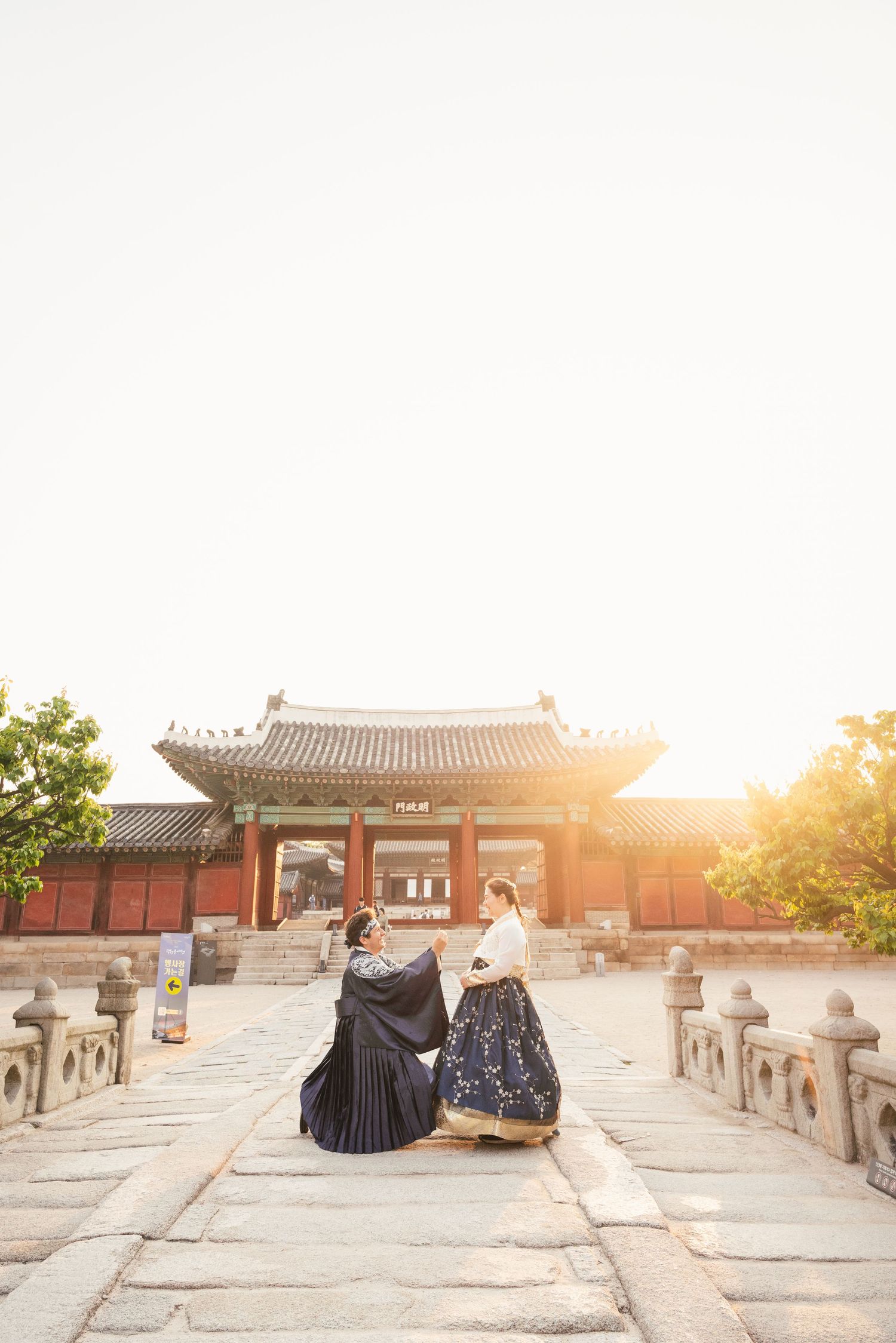 Two people sit on stone steps at the Temple of Heaven in Beijing during golden sunset hour.
