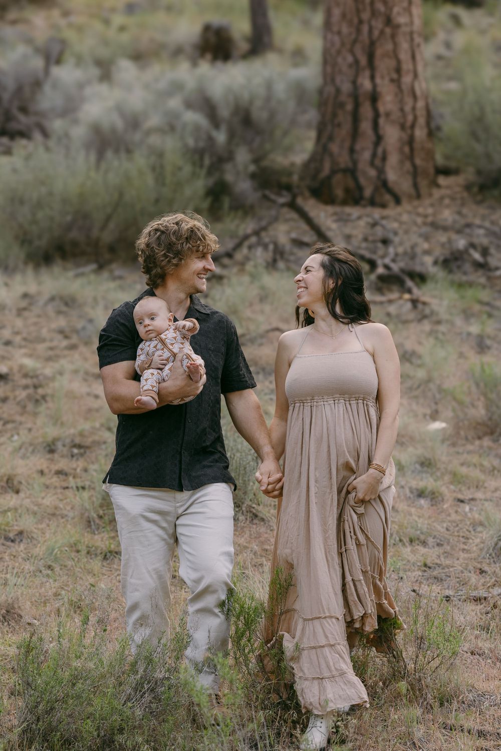 Happy young family walking through forest with father holding newborn baby and holding hands.