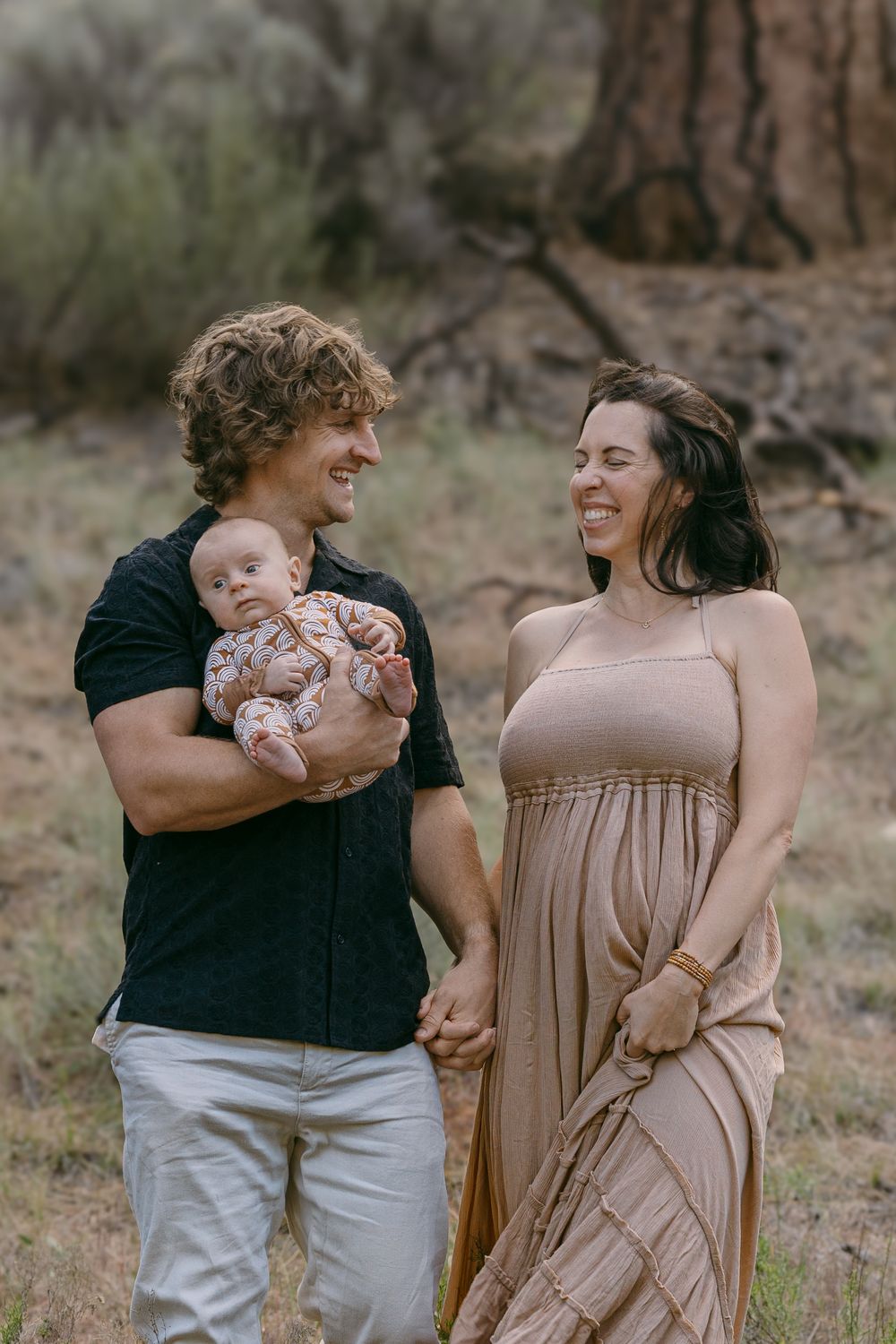 Happy young family with newborn baby walking in nature, man holding infant while couple smiles at each other.