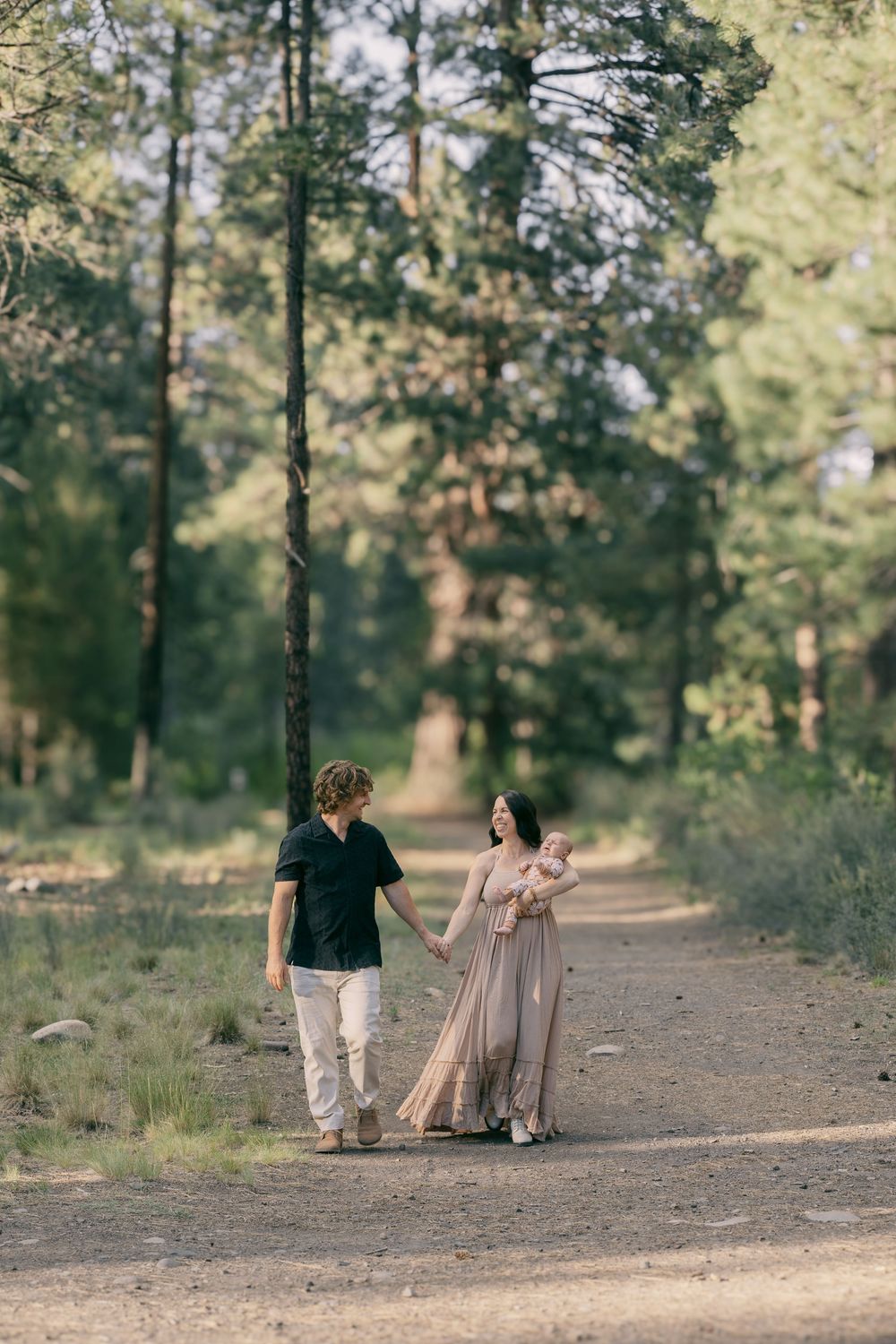 Young family walking together on a peaceful forest dirt path, mother carrying newborn baby.