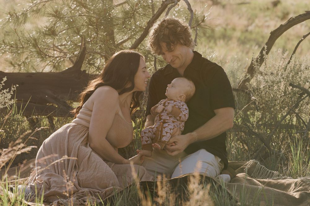 Young couple sitting in golden meadow grass lovingly attending to their newborn baby.
