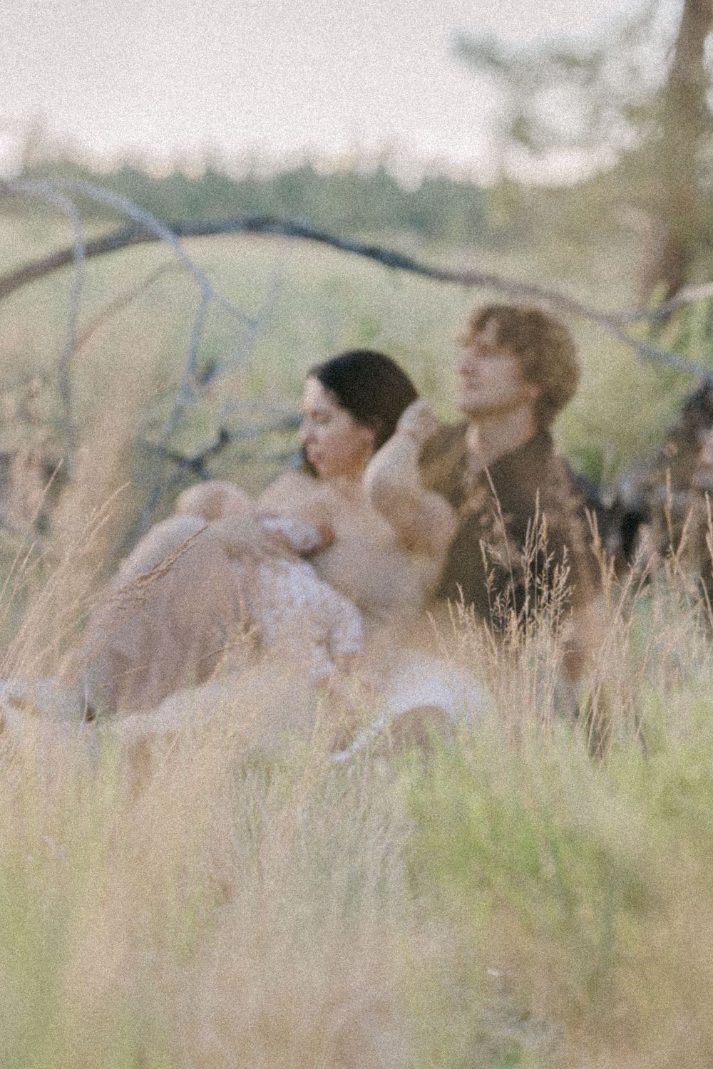Soft-focus image of couple with baby sitting in lush green meadow at dusk.