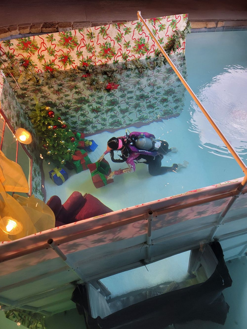 Camera equipment suspended over pool water with decorative stone wall and plants in background.