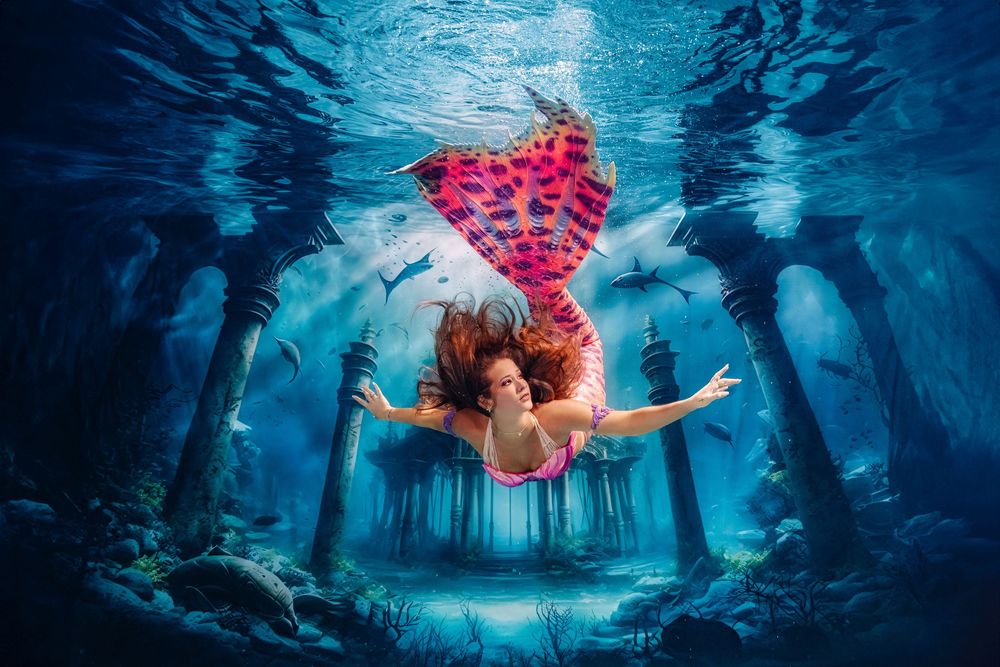 A person in a flowing red dress floats gracefully underwater in a dreamy blue aquatic scene.