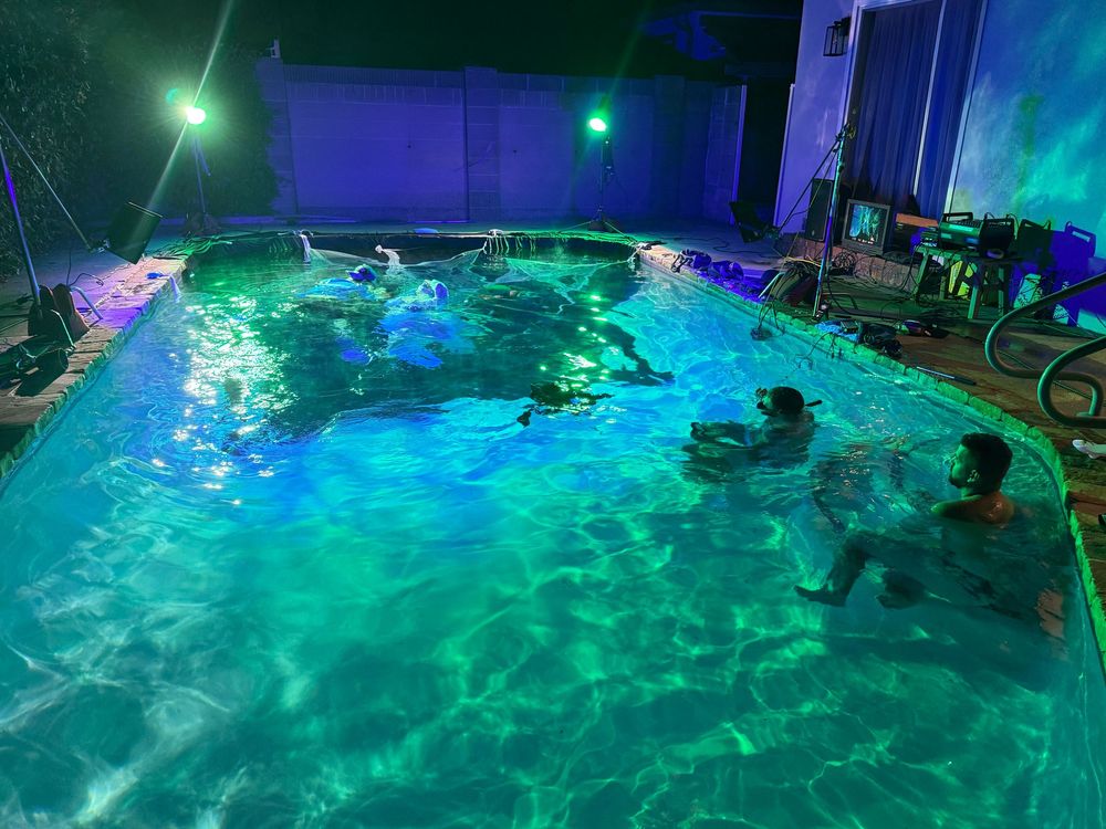 A swimming pool illuminated with colorful LED lights creating a vibrant turquoise and purple glow at night.
