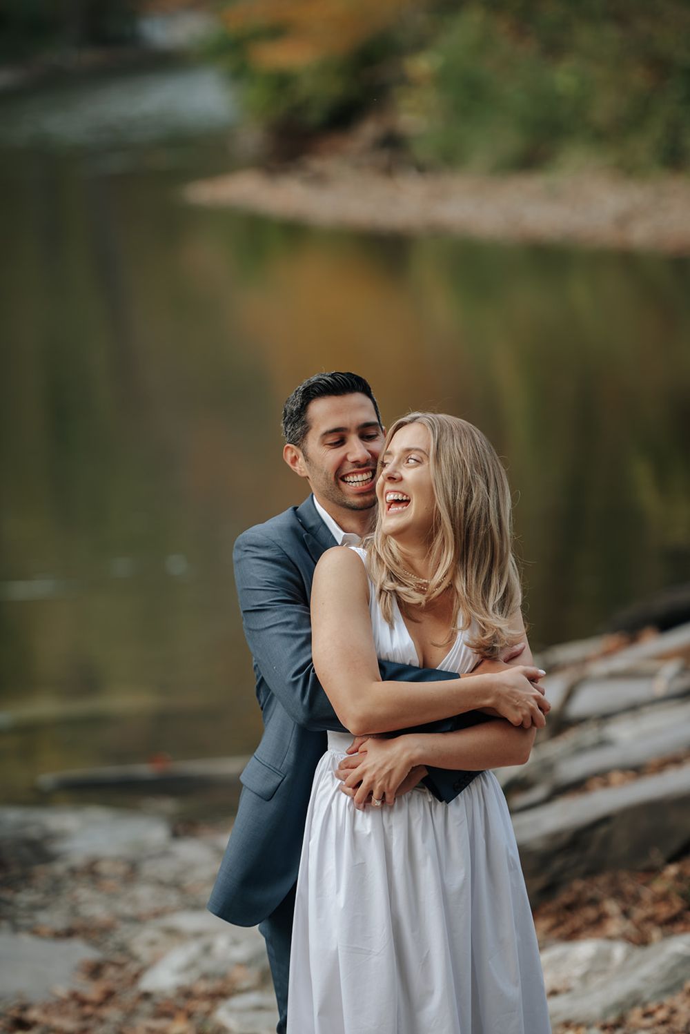 A couple shares a joyful embrace by a serene lake during their engagement photoshoot.