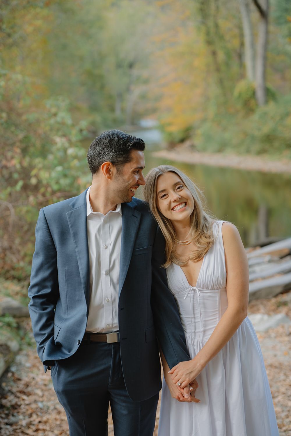 A couple shares a romantic moment together on an autumn path by a lake wearing formal attire.