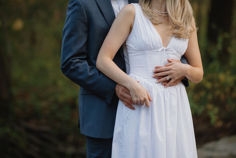 A romantic moment captured as a couple in formal attire embrace near a waterfront setting.