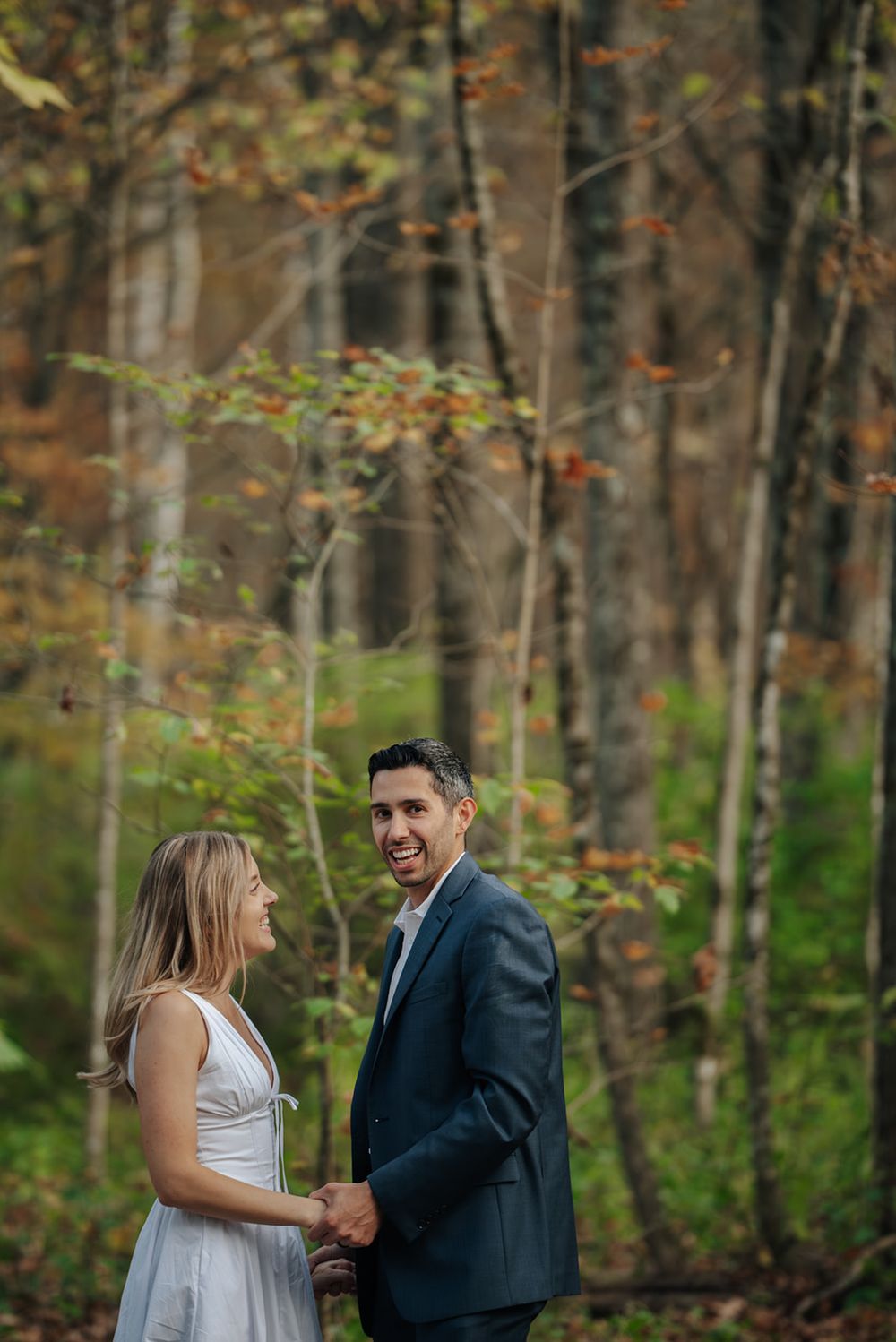 A couple shares a joyful moment together while walking through an autumn forest with golden leaves.