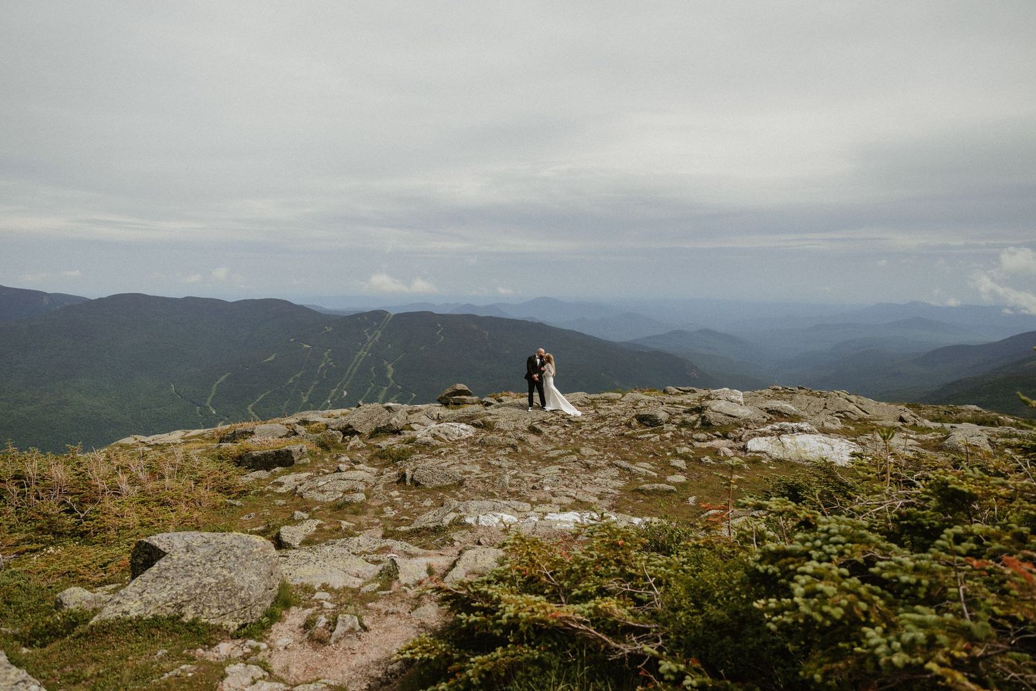 Panoramic view of mountain ranges stretching into the distance with rocky terrain in foreground.
