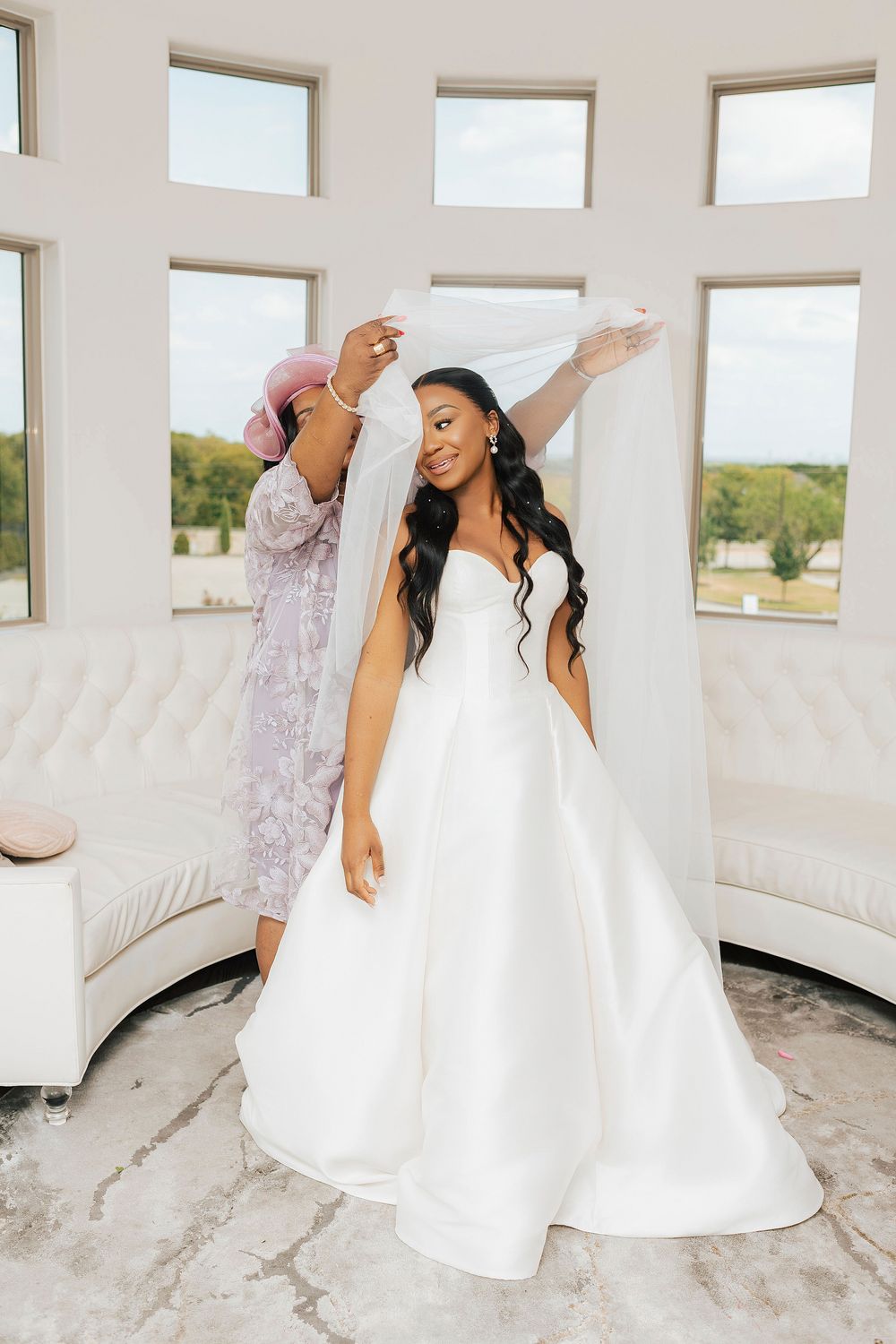 A bride in a white wedding dress dances joyfully in a bright white room with small windows.
