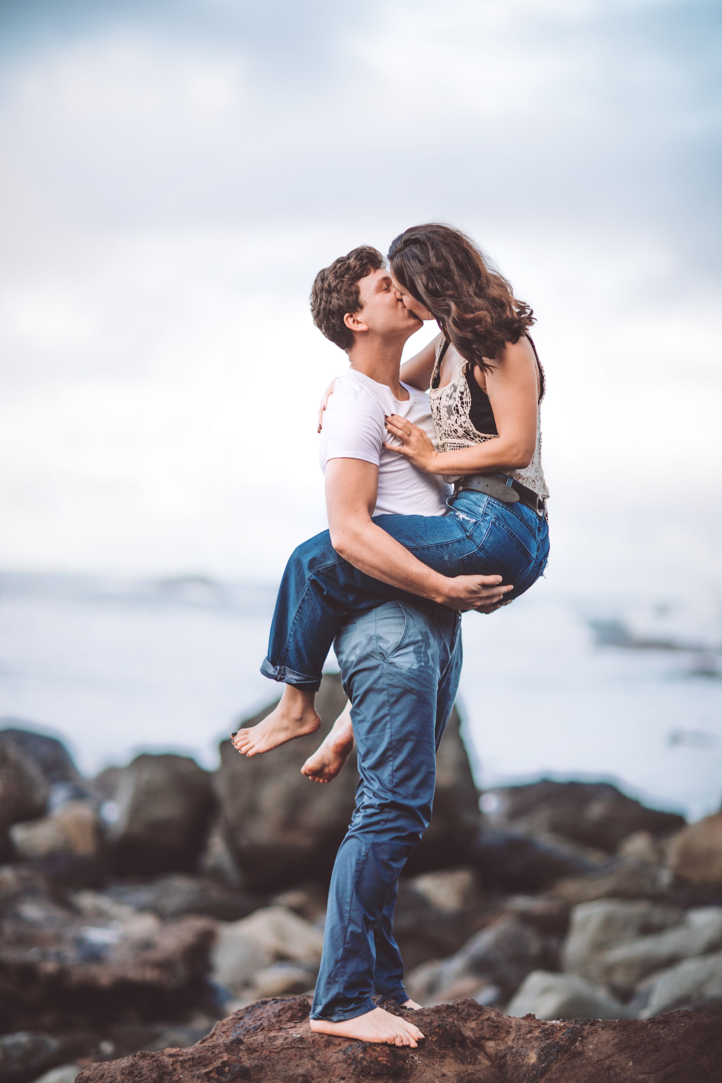 A loving couple shares playful moments on rocky coastal cliffs overlooking the ocean.