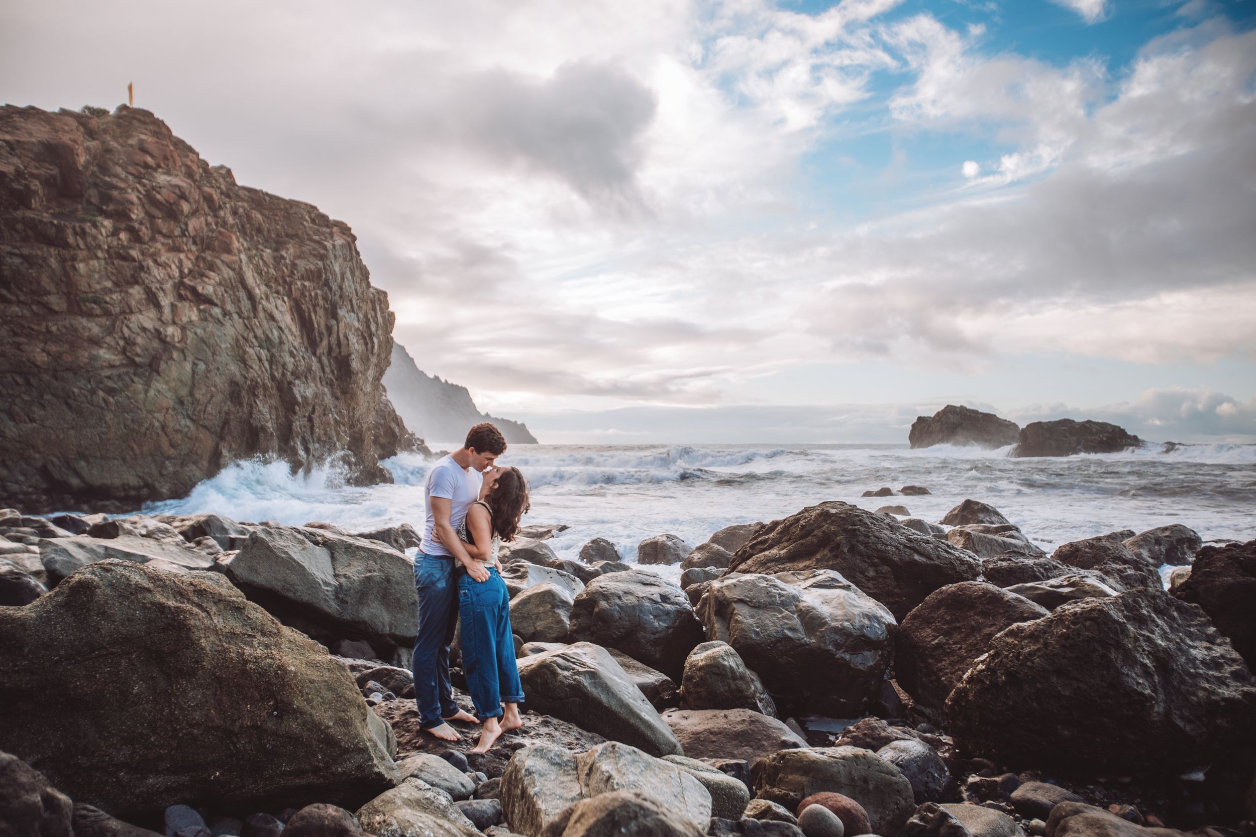 Dramatic coastal landscape with rocky shore and cloudy skies during an engagement session.