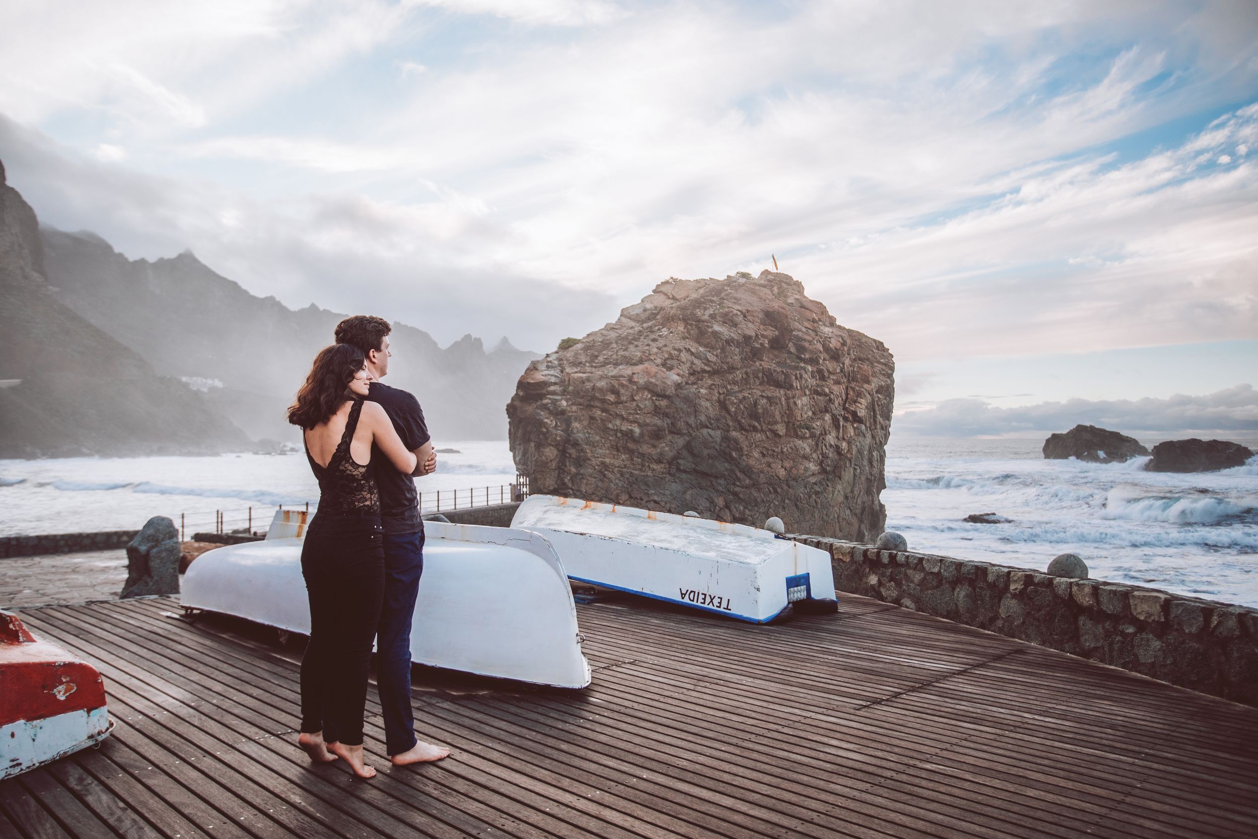 An intimate moment captured on a scenic coastal boardwalk with mountain and ocean views.