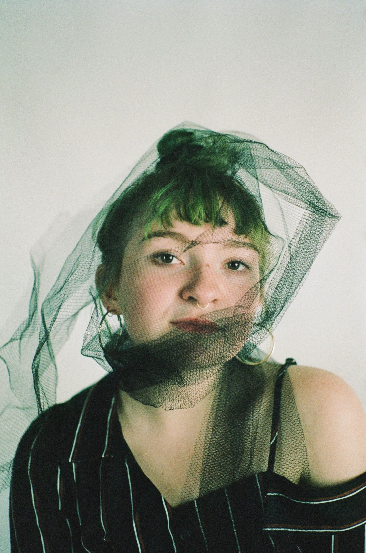 Artistic portrait series with green tulle veil and striped clothing against white background.