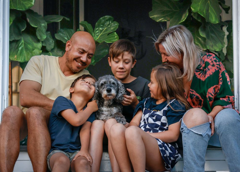 Family gathering on a porch with greenery and white railings visible in background.