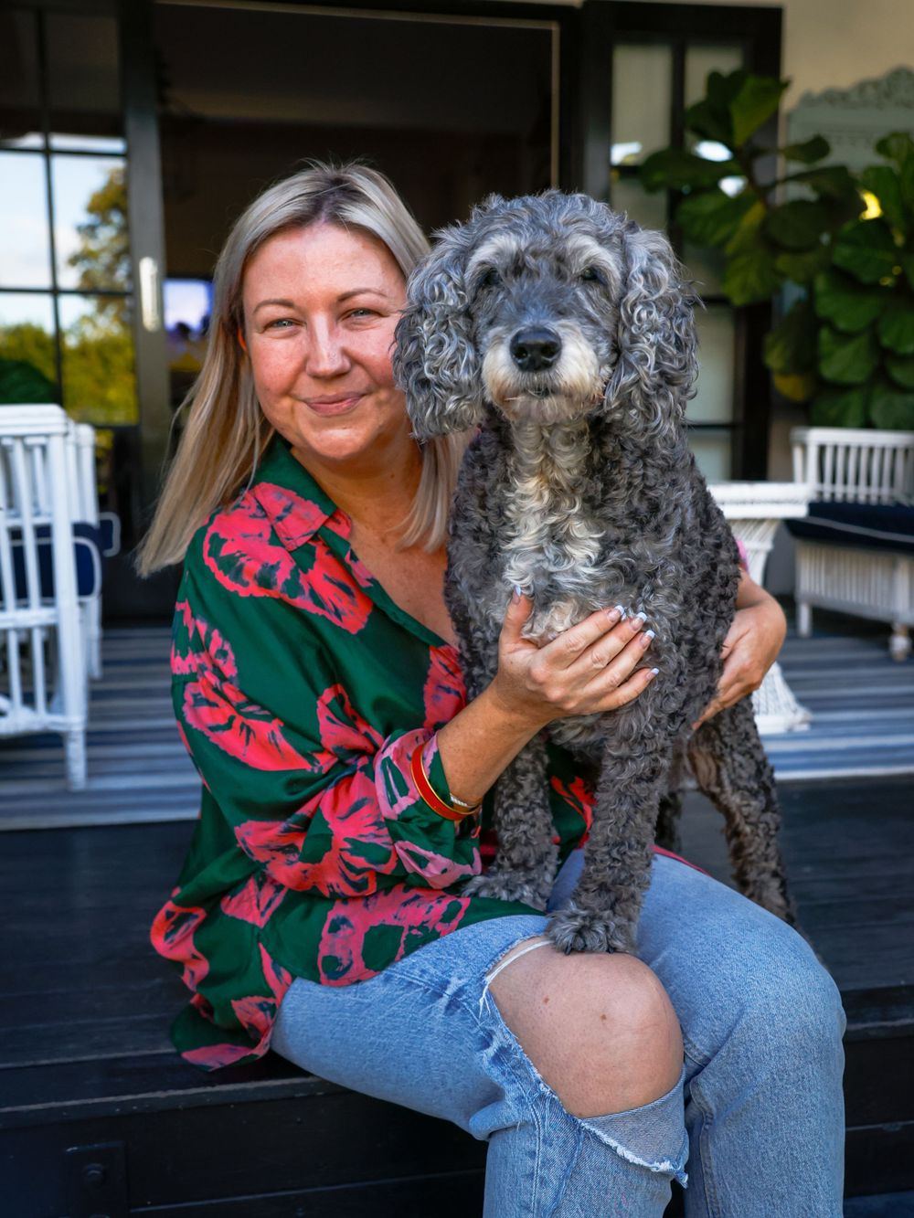 Gray poodle mix dog being held while sitting on a porch with people.