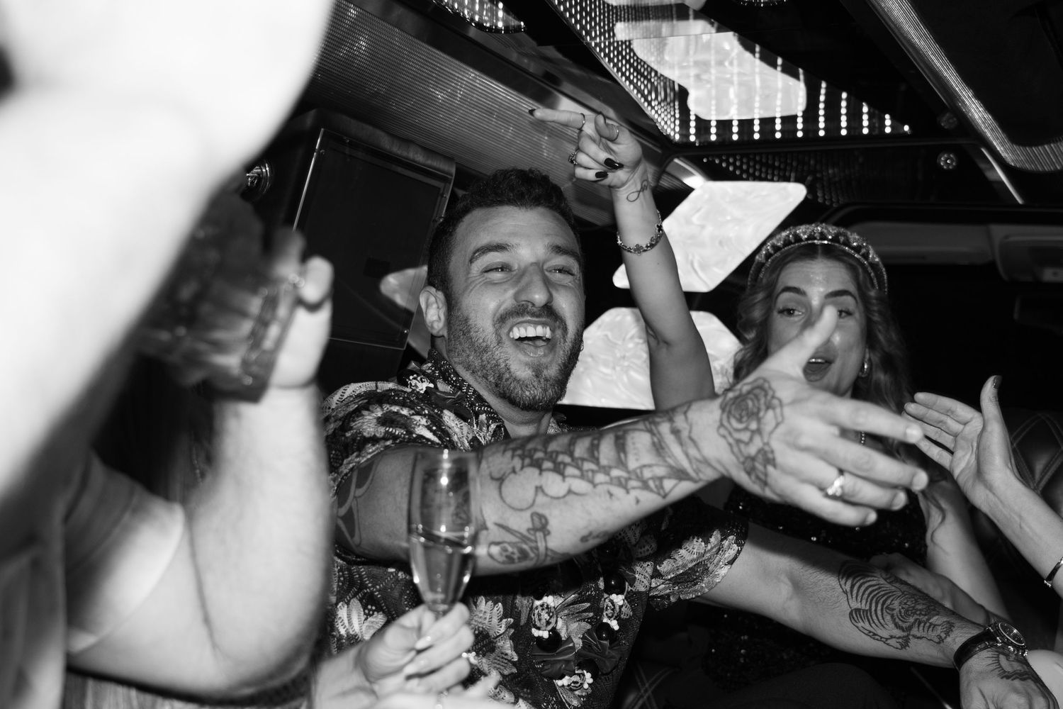 Black and white photo of tattooed man celebrating at lively party holding champagne glass in Hawaii.