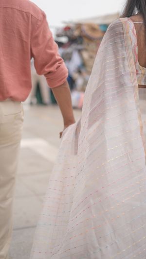 Close-up detail of a delicate white sari with pink accents next to a salmon-colored shirt and khaki pants.