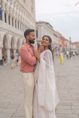 A couple shares a romantic moment under historic arches in Venice wearing coral and cream colored outfits.