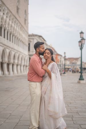 Romantic couple shares an intimate moment along the historic colonnades of St. Mark's Square in Venice.