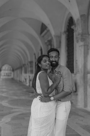 A couple embraces in black and white under arched colonnade walkway in Venice, Italy.