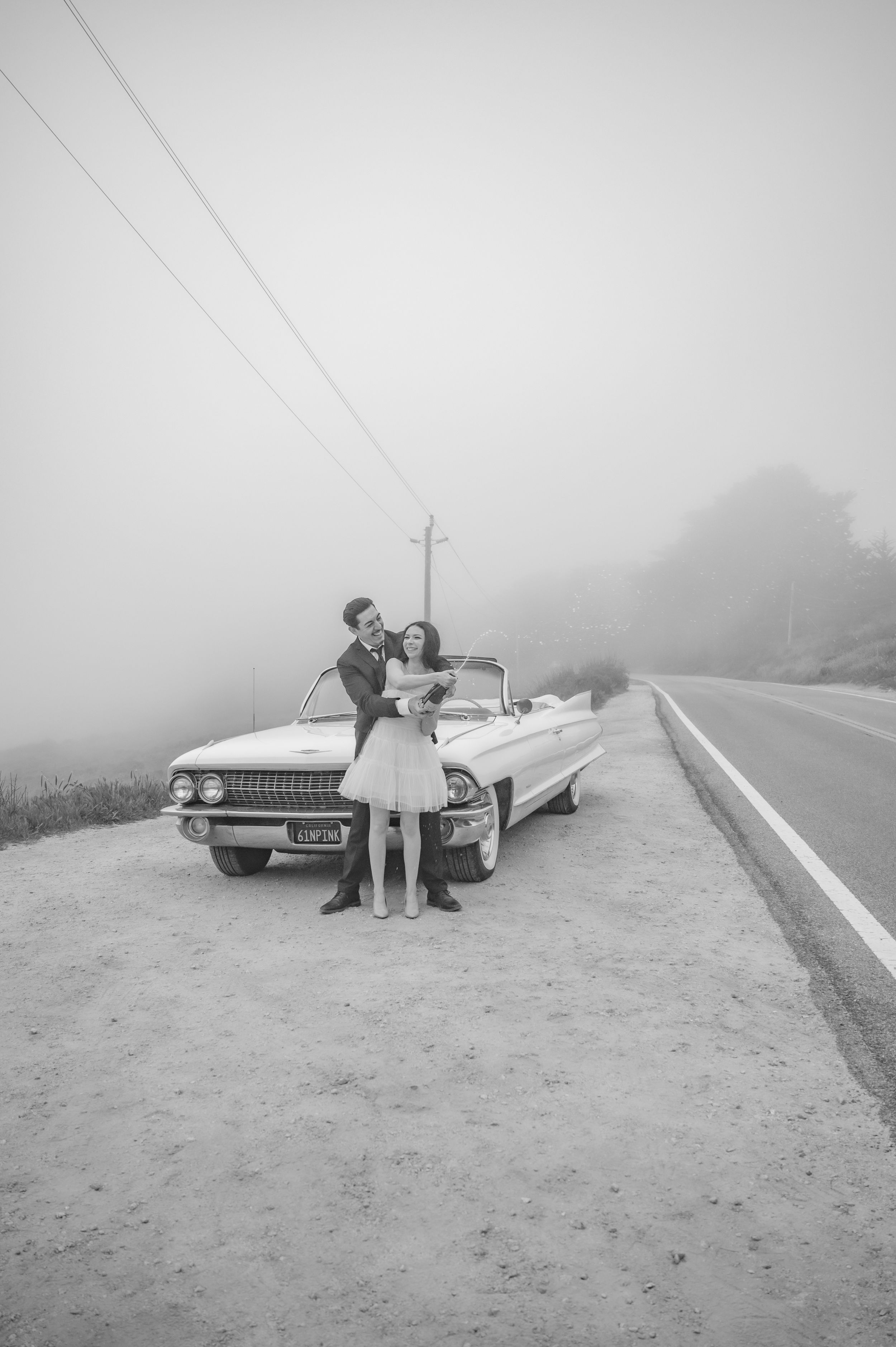 A dreamy vintage scene with a couple beside a classic white Cadillac convertible on a foggy mountain road.
