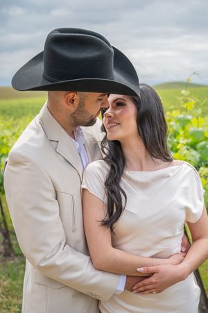 A romantic couple embraces in a field of wildflowers, with one wearing a black cowboy hat and cream suit.