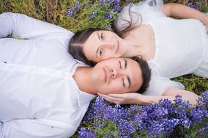 A couple in white clothing lying down in a field of purple lavender flowers on a sunny day.