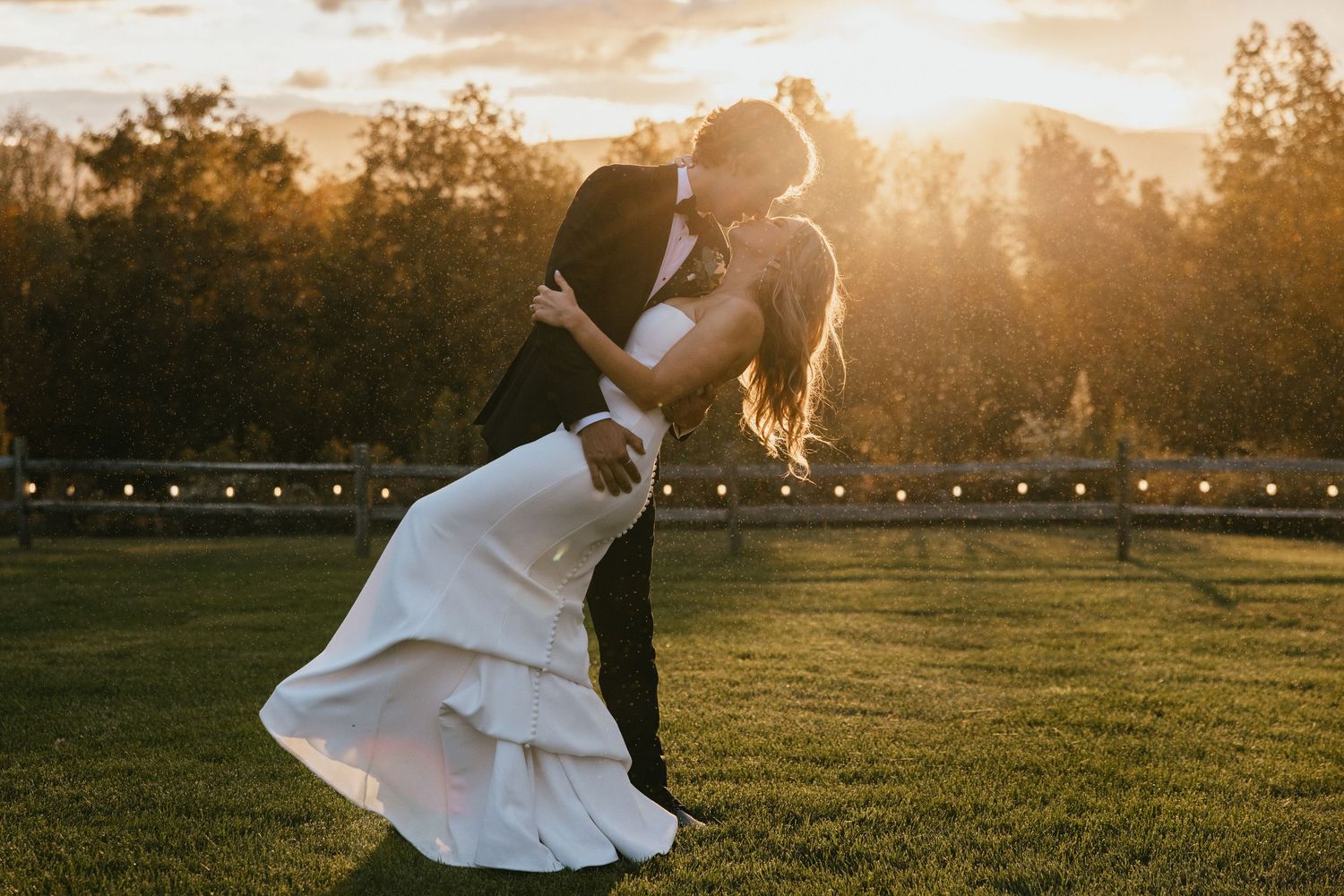 A couple embraces in a golden sunlit field during sunset creating a romantic silhouette against the warm sky.