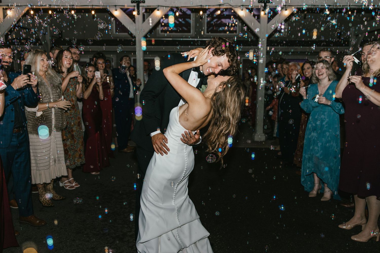 Wedding guests dance and celebrate on a dark dance floor under twinkling lights during an evening reception.