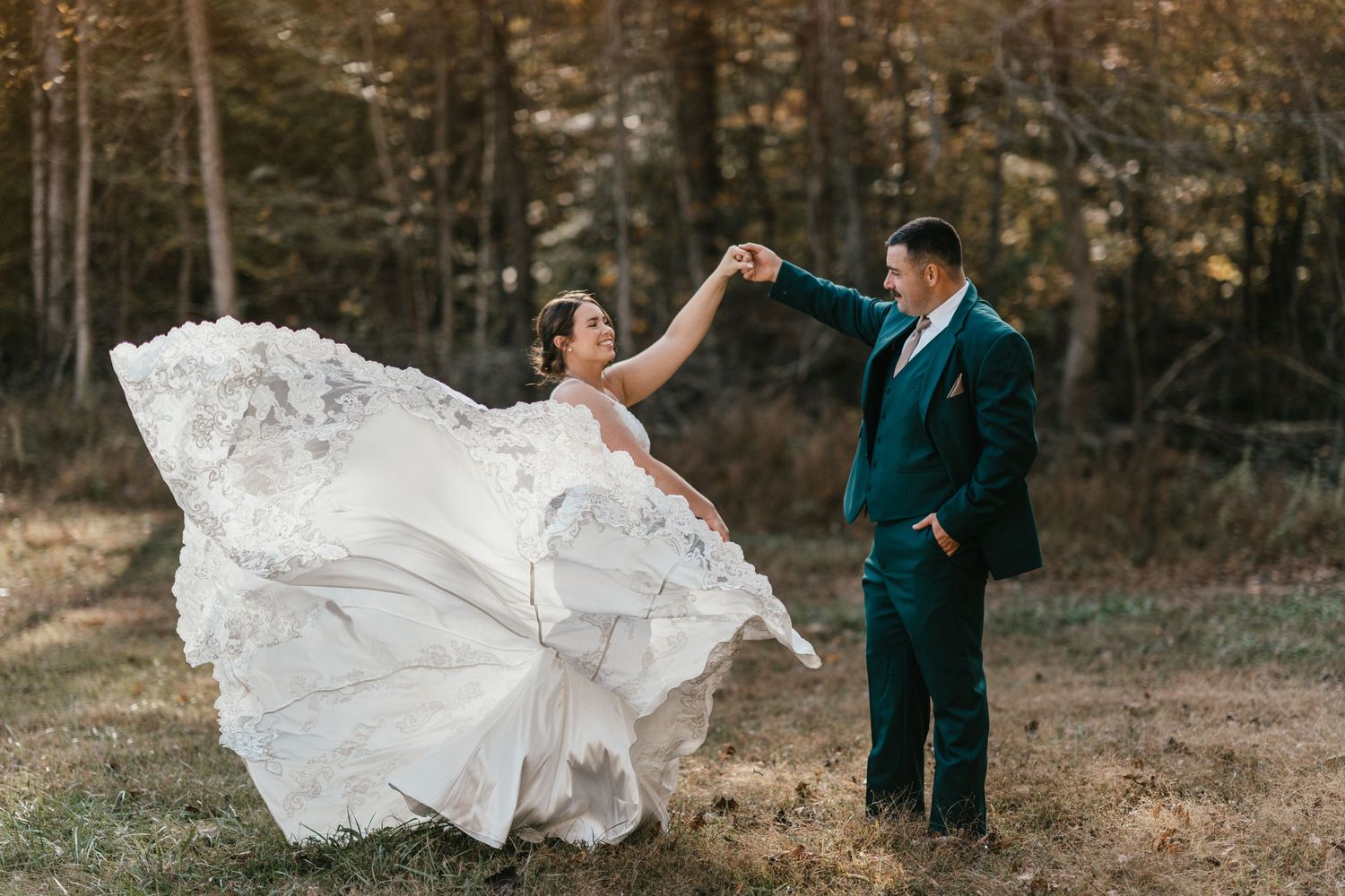 A couple in wedding attire stands in an autumn forest as the bride's white dress flows elegantly in the breeze.