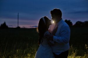 Couple sharing a romantic embrace at sunset in a field, silhouetted against a purple twilight sky.