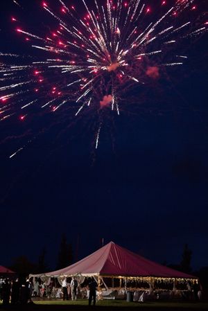 Pink fireworks exploding over a red event tent at night during an outdoor celebration.