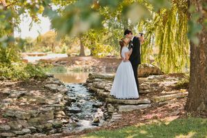 Bride and groom share a romantic kiss by a stone creek in a lush garden setting on their wedding day.