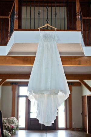 A white lace wedding dress hanging on a wooden hanger in an elegant rustic venue with wooden balcony.