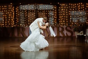 Newlyweds share romantic first dance dip in front of glowing fairy lights and Mr & Mrs sign at wedding reception.