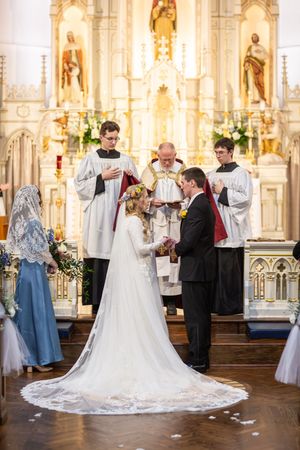 Bride and groom exchange vows at ornate church altar with priest and altar servers during traditional wedding ceremony.