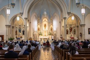 Congregation gathered in an ornate Catholic church during Mass, featuring a grand white altar and Gothic architecture.
