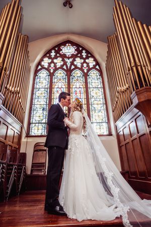 Bride and groom sharing a kiss at the altar of a church with stained glass windows and pipe organ.