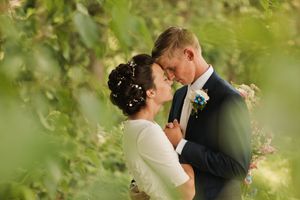 A bride and groom share a romantic moment surrounded by lush green foliage on their wedding day.