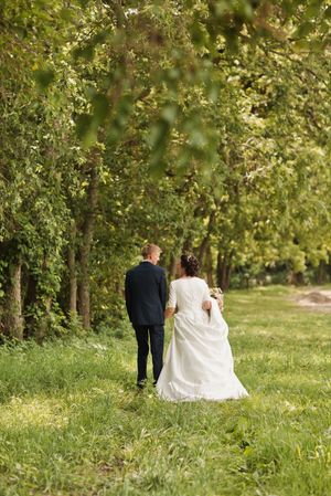 A bride and groom walk hand in hand through a lush green forest path on their wedding day.