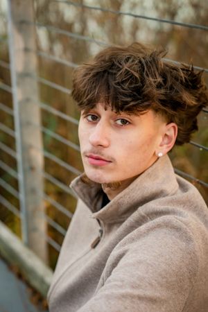 Close-up portrait of person in beige sweatshirt against metal railing outdoors.