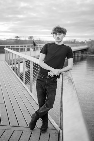 Black and white photo of person in casual wear leaning against railing on wooden deck.